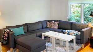 Un salon moderne avec un canapé d’angle, une table basse blanche et un tapis moelleux.