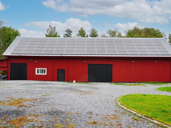 A red barn with a gravel driveway and a solar panel roof.