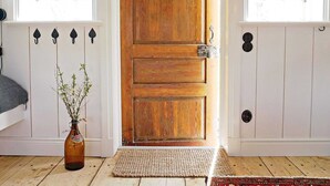 A wooden door with a metal latch, a woven doormat, and a bottle of beer on the floor. - 5 Person Holiday Home in Mellosa (Flen)