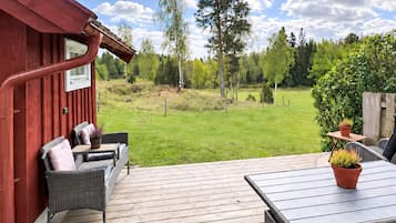A wooden deck with outdoor furniture, a red building, and a grassy yard with trees.