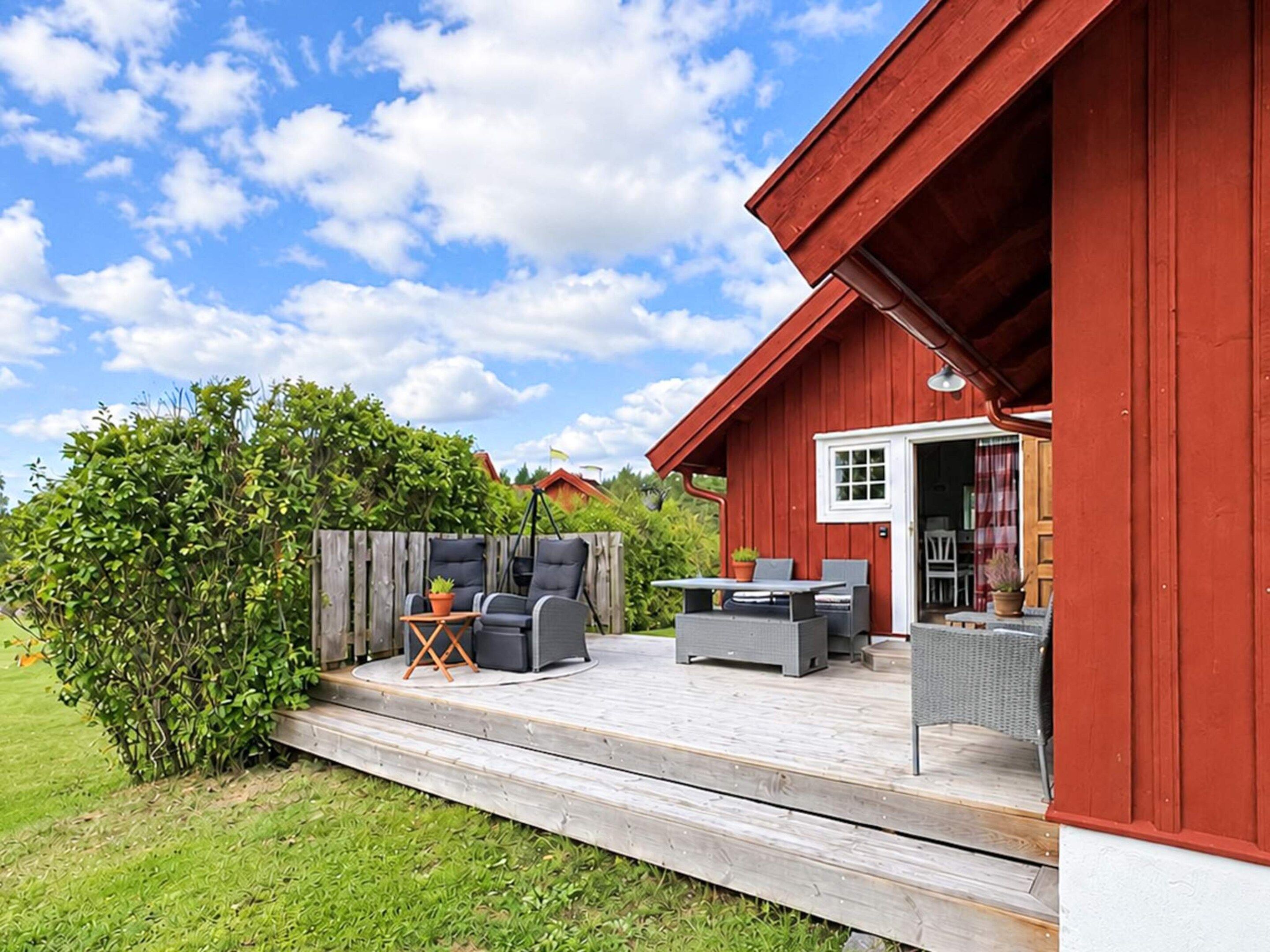 A red wooden building with a deck, outdoor seating, and a view of a green landscape.