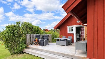 A red wooden building with a deck, outdoor seating, and a view of a green landscape.