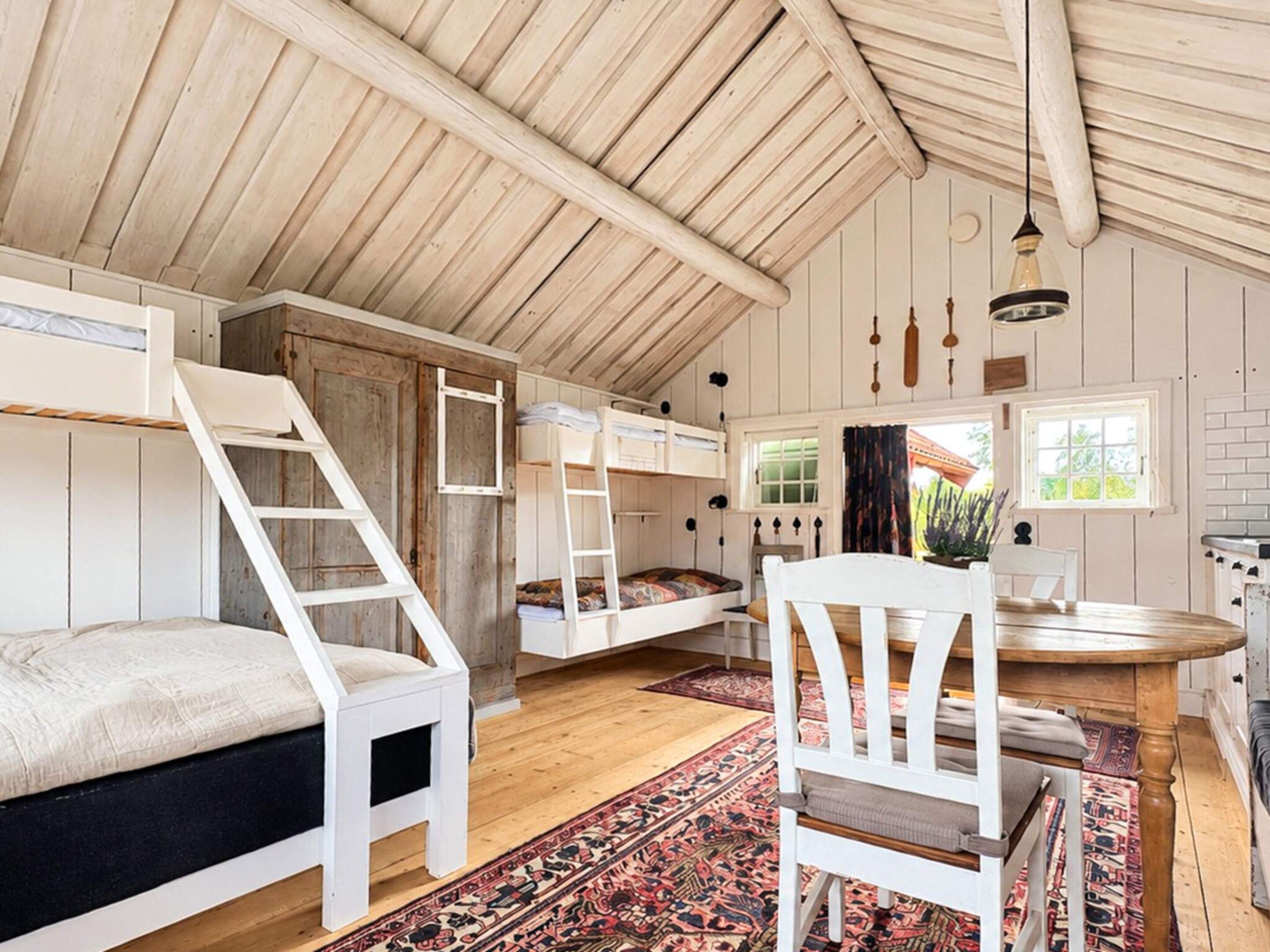 A cozy attic bedroom with bunk beds, a wooden ceiling, and a dining area with a table and chairs.