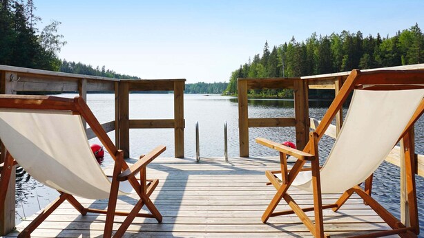 A wooden deck with two canvas chairs facing a calm lake, surrounded by trees. - 5 Person Holiday Home in Mellosa (Flen)