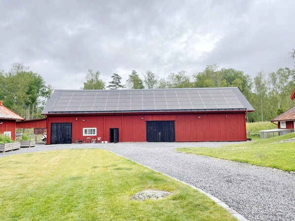 A red barn with a gravel driveway leading to a black door.