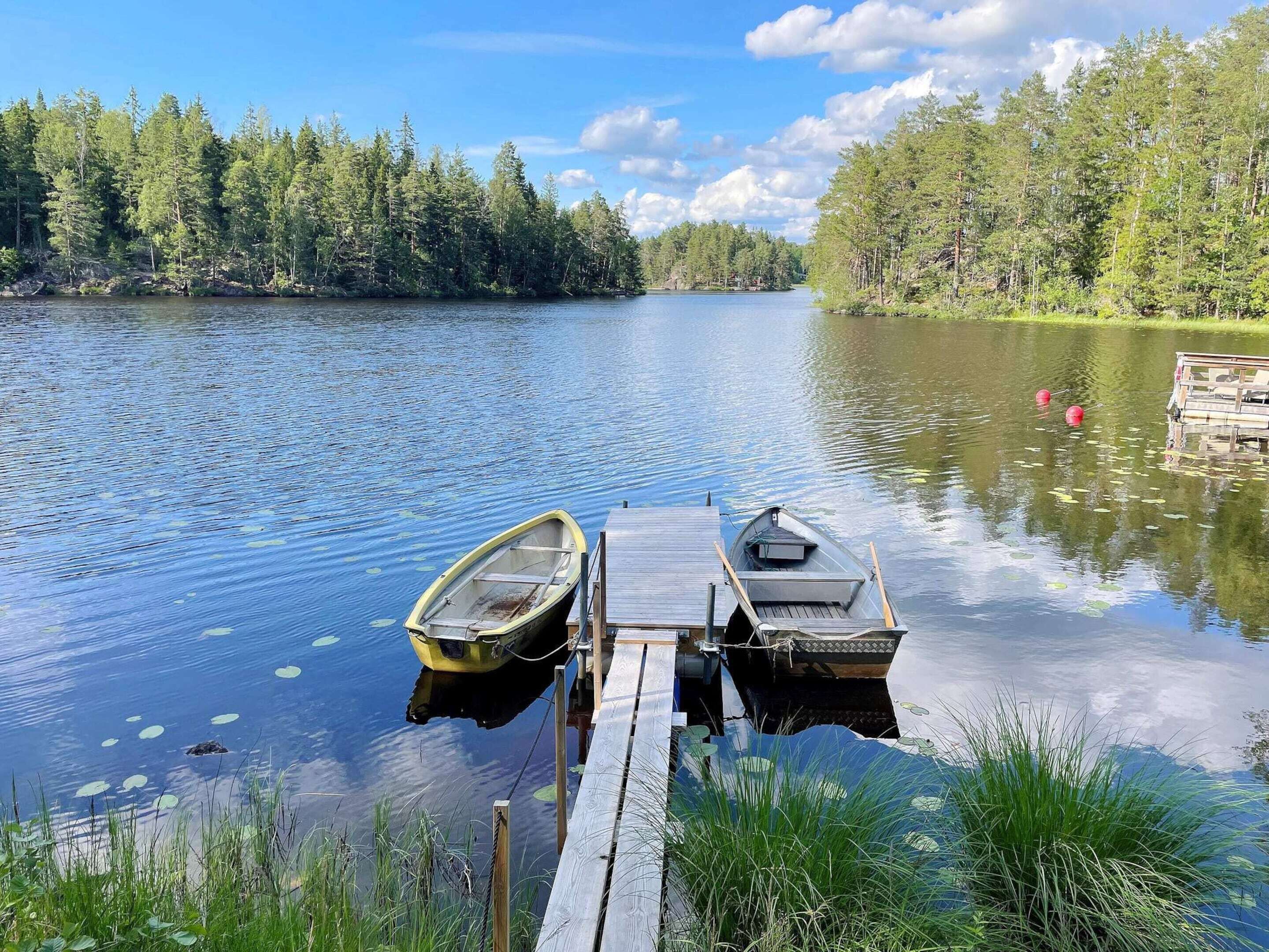 A calm lake with two boats docked at a wooden pier, surrounded by dense forest.