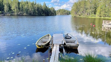 A calm lake with two boats docked at a wooden pier, surrounded by dense forest.