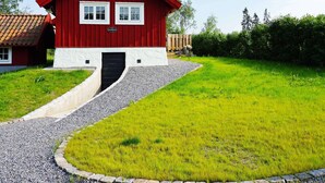 A red wooden house with a white base, a black door, and a gravel driveway leading to the entrance. - 5 Person Holiday Home in Mellosa (Flen)