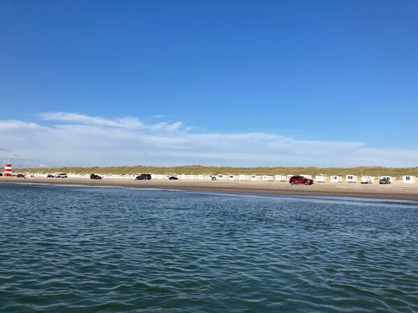 A beach with a row of caravans and a lighthouse in the background.