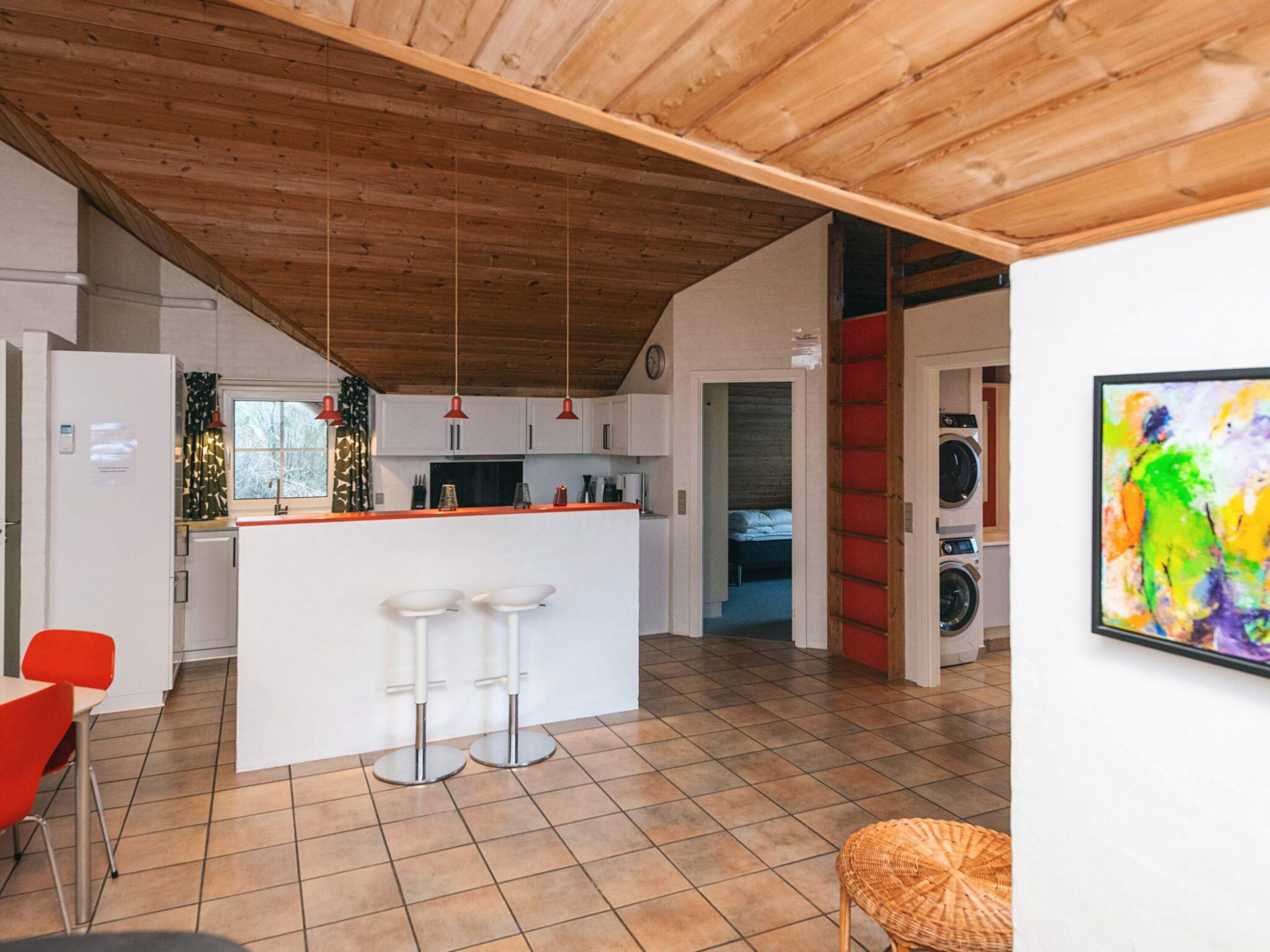 A modern kitchen with a central island, bar stools, and a dining area with a red chair.