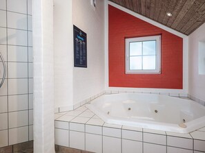 A bathroom with a white bathtub, a red accent wall, and a small window. - Holiday Home in Blåvand (Blavand)
