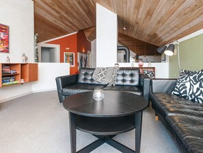 A modern living room with a black leather sofa, a round coffee table, and a bookshelf. - Holiday Home in Blåvand (Blavand)