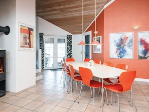A dining area with a white table and orange chairs, a fireplace, and artwork on the walls. - Holiday Home in Blåvand (Blavand)