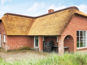 A brick building with a thatched roof, a brick chimney, and a paved entrance area. - Holiday Home in Blåvand (Blavand)