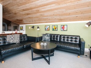 En moderne stue med en lædersofa i kodelook, et rundt sofabord og et køkken i baggrunden.
