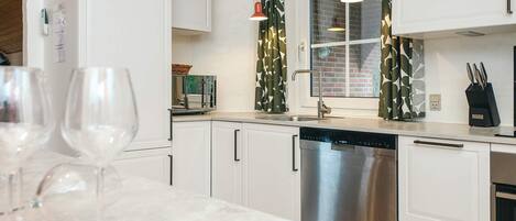 A modern kitchen with white cabinetry, stainless steel appliances, and a marble countertop.