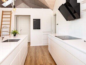 A modern kitchen with white cabinetry, a stainless steel sink, a wooden ladder, and a potted plant.