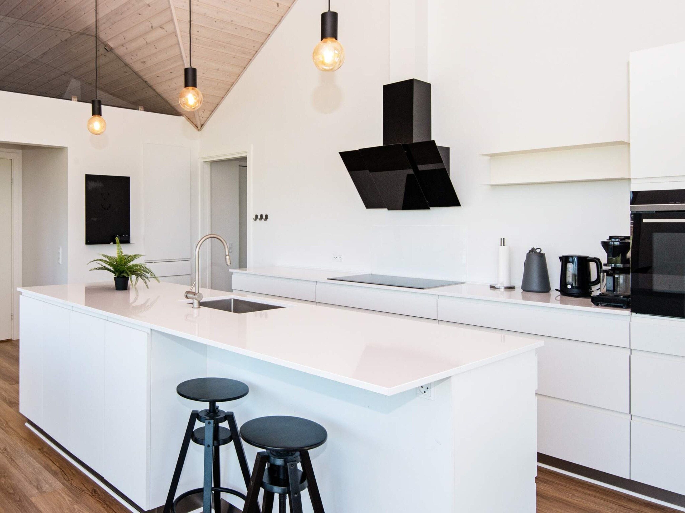 A modern kitchen with a central island, bar stools, a black range hood, and pendant lighting.