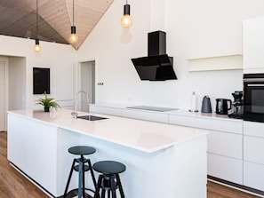 A modern kitchen with a central island, bar stools, a black range hood, and pendant lighting. - Holiday Home in Odder (Odder)