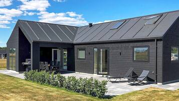 Ein modernes Haus mit Satteldach, großen Fenstern und einer Terrasse mit Gartenmöbeln.