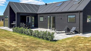 Ein modernes Haus mit Satteldach, großen Fenstern und einer Terrasse mit Gartenmöbeln.