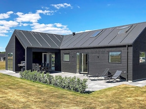 A modern house with a sloped roof, large windows, and a patio area with outdoor furniture. - Holiday Home in Odder (Odder)