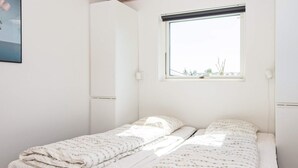 Una cama individual con colcha blanca y estampado floral, cabecera negra y ventana con vistas al exterior.
