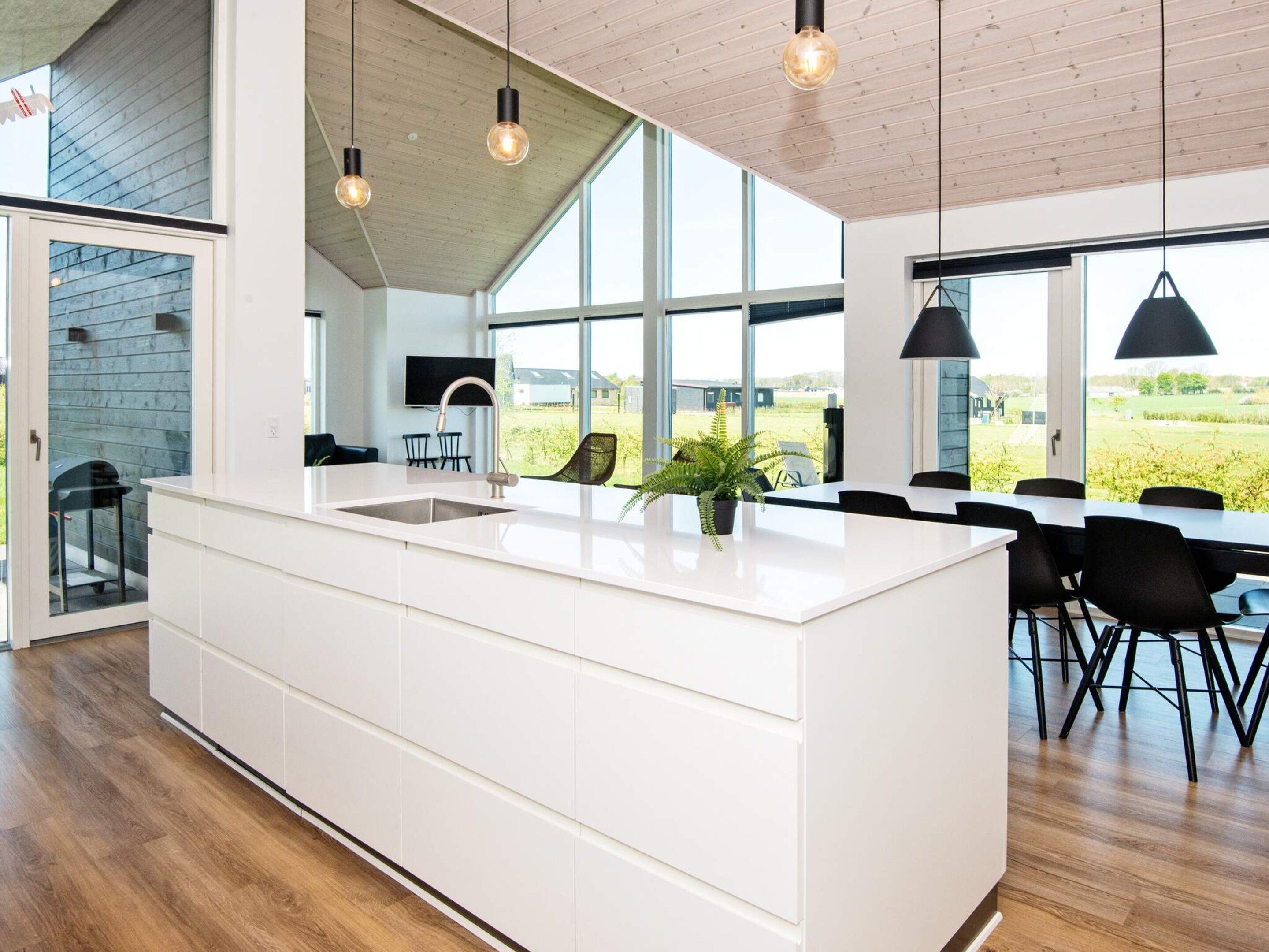 A modern kitchen with a large island, wooden flooring, and large windows offering a view of the outdoors.