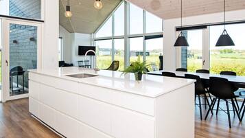 A modern kitchen with a large island, wooden flooring, and large windows offering a view of the outdoors.