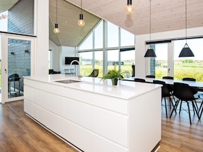 A modern kitchen with a large island, wooden flooring, and large windows offering a view of the outdoors. - Holiday Home in Odder (Odder)