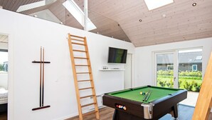Una habitación moderna con mesa de billar, televisor montado en la pared y un ventanal con vistas al exterior.