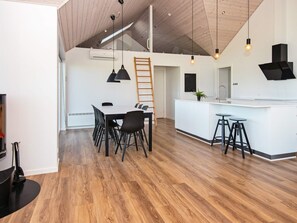 A modern kitchen with a wooden ceiling, a dining area with a table and chairs, and a bar area with stools.