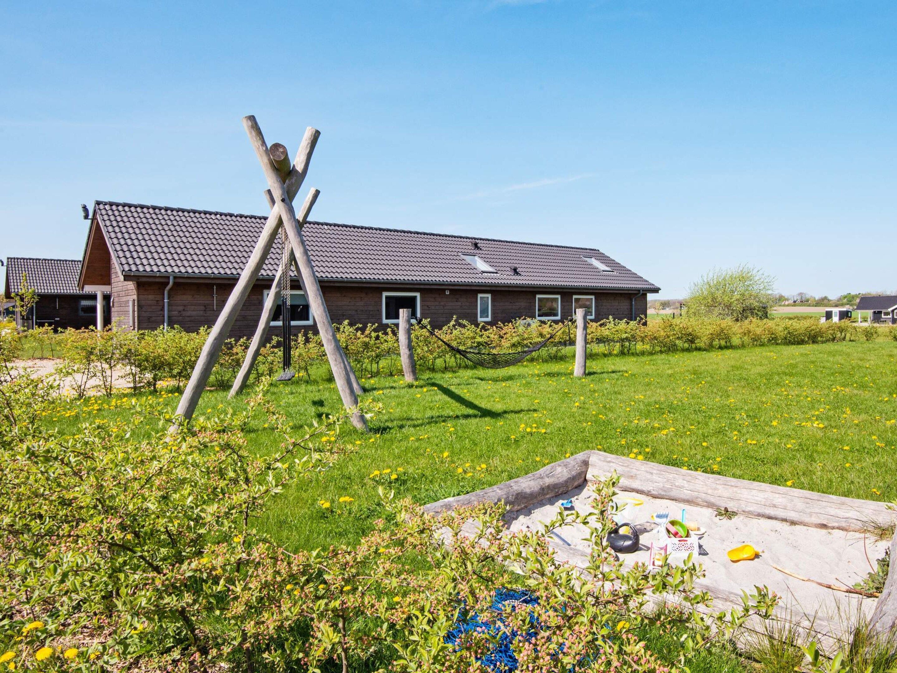 A building with a sloped roof, wooden beams, and a grassy field with a hammock.