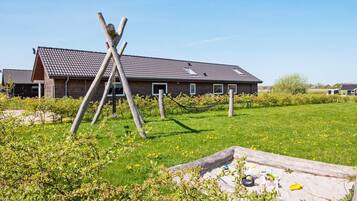 A building with a sloped roof, wooden beams, and a grassy field with a hammock.