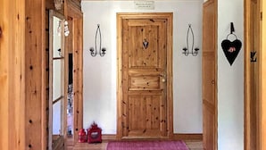 Um corredor de madeira com uma porta central, um pequeno banquinho e uma sacola vermelha no chão.
