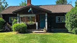 Uma casa de dois andares com telhado em telhas, chaminé e varanda frontal.