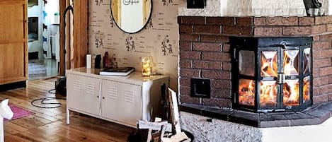 A room with a fireplace, wooden flooring, a mirror on the wall, and a small table with items on it.