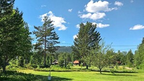 Um campo gramado com árvores e alguns edifícios ao fundo.