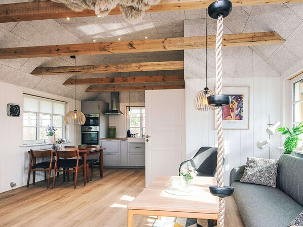 A cozy kitchen with wooden beams, a dining area with a table and chairs, and a living area with a sofa and a plant. - 4 Person Holiday Home in Ulfborg (Ulfborg)