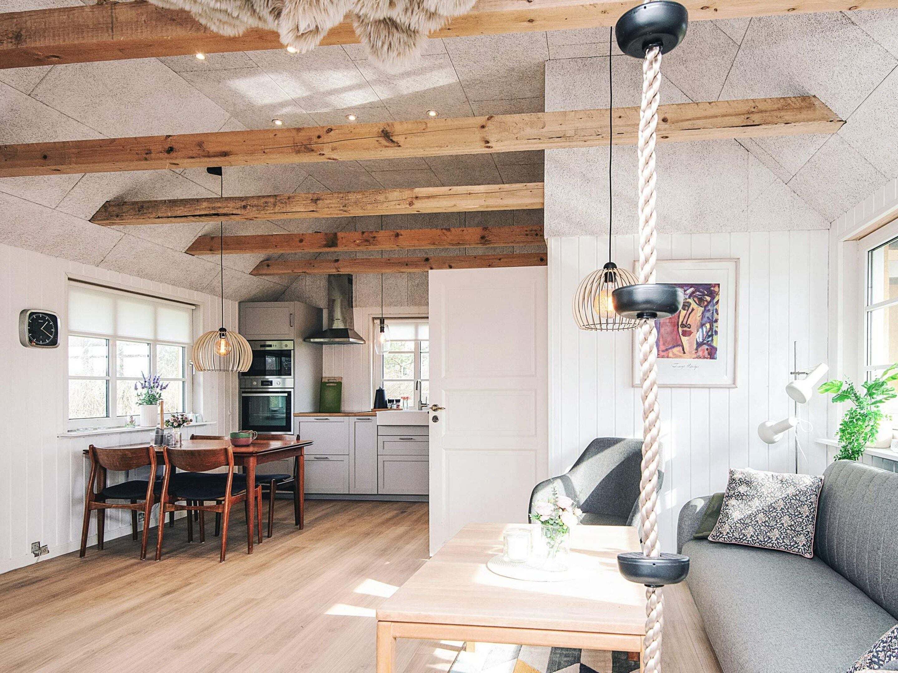 Une cuisine chaleureuse avec des poutres en bois, un coin repas avec une table et des chaises, et un salon avec un canapé et une plante.