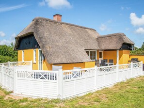 Een rieten dak huis met een witte omheining, een gele buitenmuur en een schoorsteen.