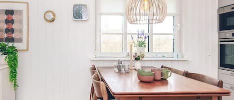 A dining area with a wooden table, chairs, a hanging light fixture, and a window with a view.