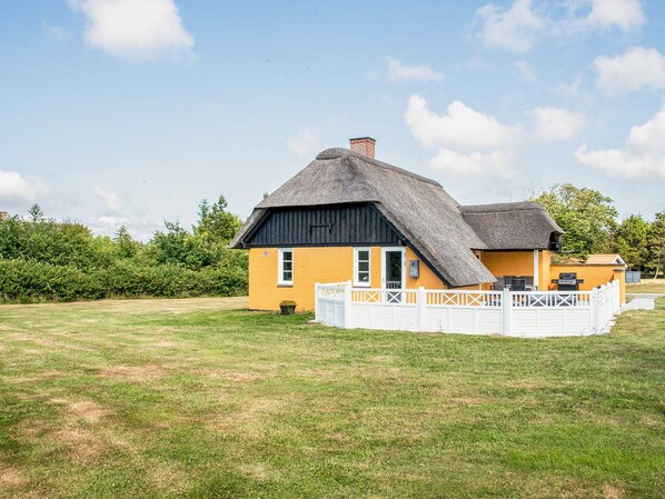 A single-story house with a thatched roof, a fenced yard, and a clear sky.