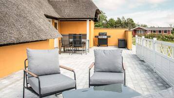 Une terrasse extérieure avec deux fauteuils gris, une petite table et un barbecue.