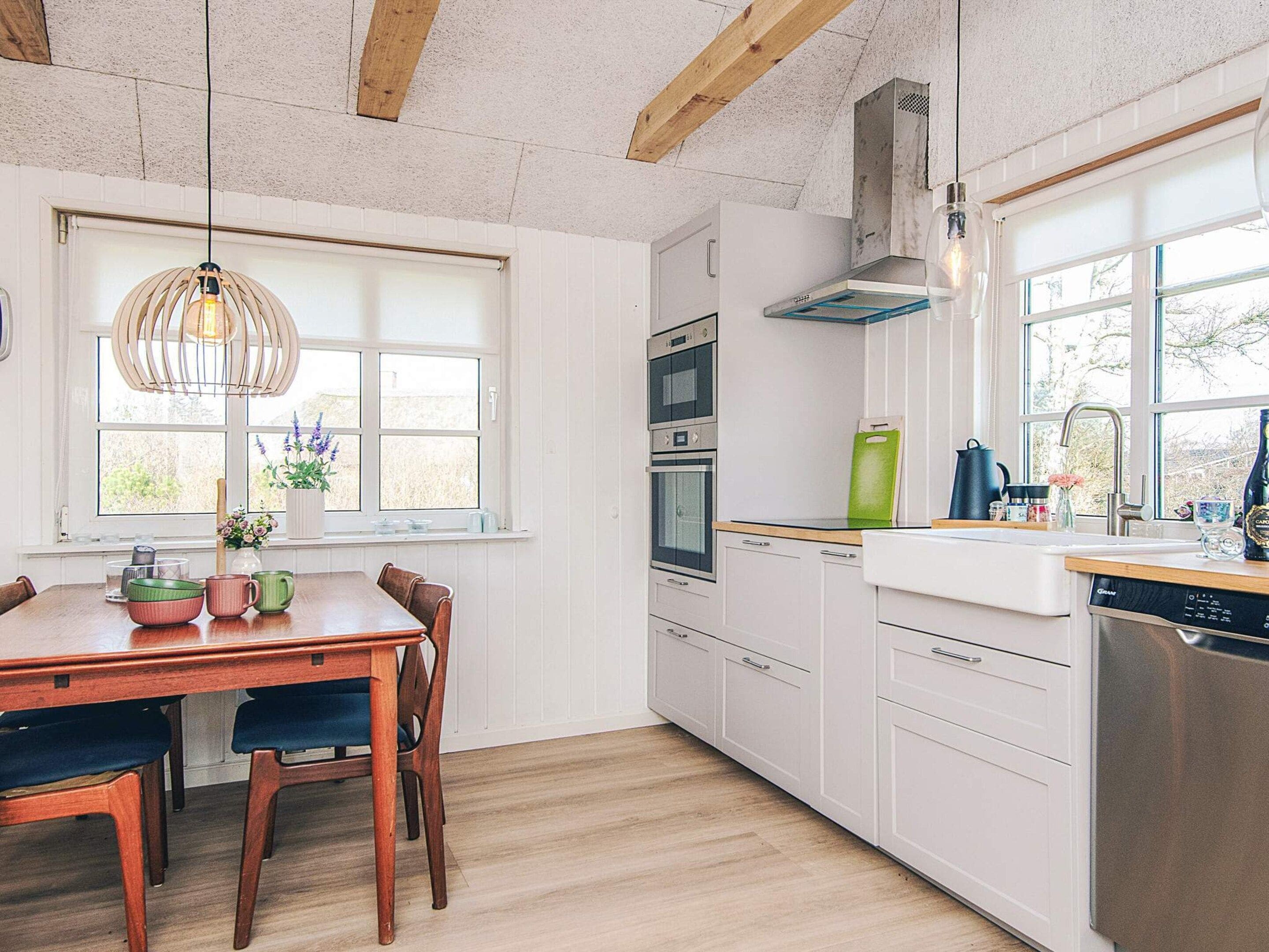 Une cuisine moderne avec des meubles blancs, une table à manger en bois et un four encastré.