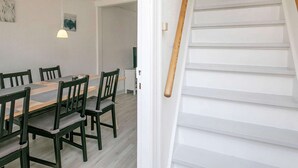 Ein Essbereich mit Holztisch und -stühlen, einer Pendelleuchte und einer Treppe mit weißen Geländern.