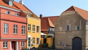 Ein Kopfsteinpflasterhof mit bunten Gebäuden, darunter ein rotes und gelbes Haus mit einer roten Tür sowie ein Ziegelgebäude mit einer dunklen Tür.