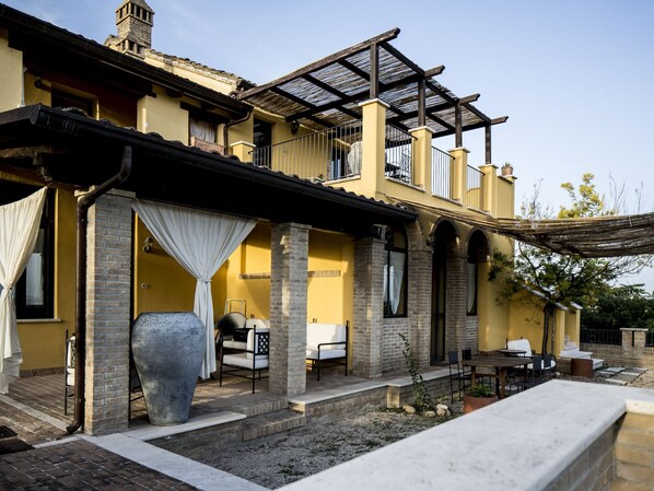 A two-story house with a patio area, outdoor seating, and a large planter.