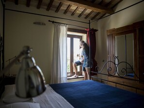 A bedroom with a bed, a window with curtains, a bedside lamp, and a wooden ceiling.