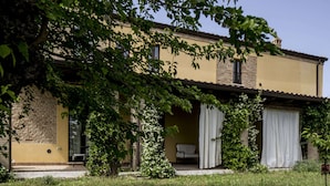 A two-story building with a yellow facade, a brick lower level, and a covered patio area with white curtains. - Hillside Retreat in San Savino (Ripatransone)
